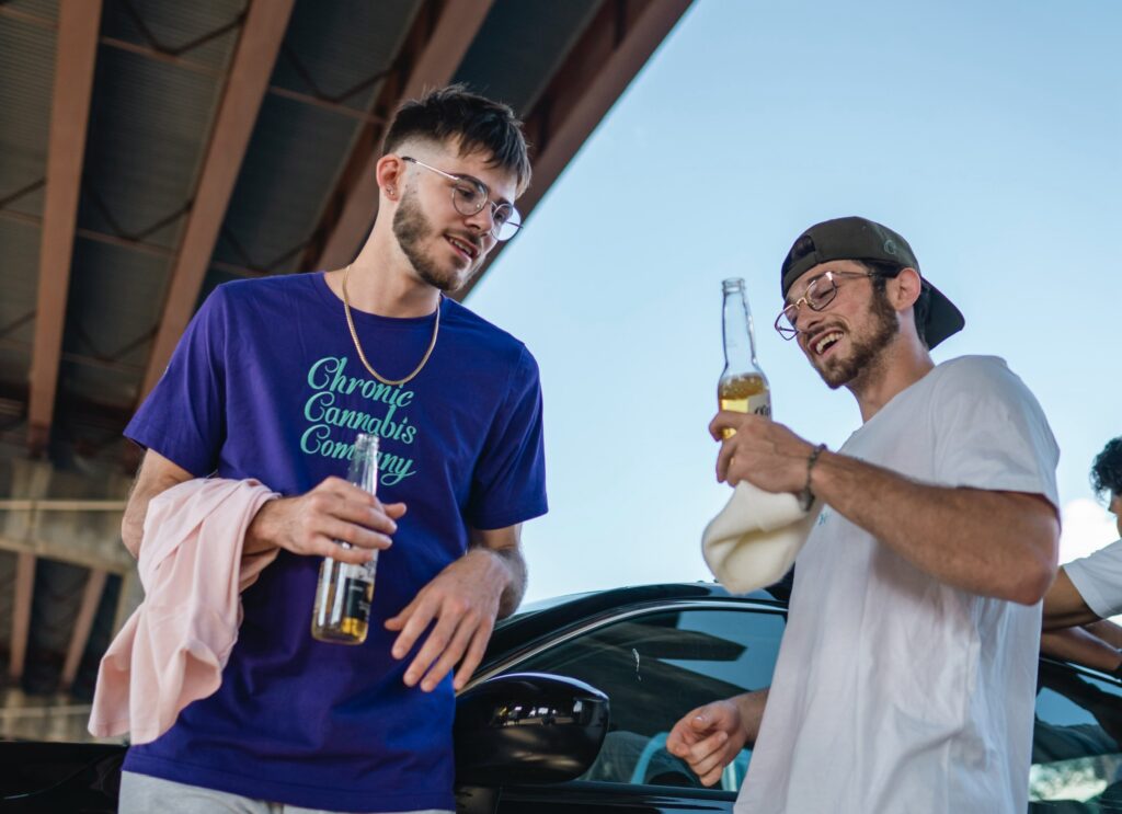 Two men laughing and drinking beer outdoors.