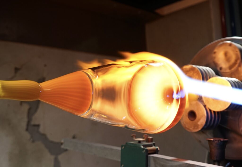Glassblowing process with hot glass and flames.