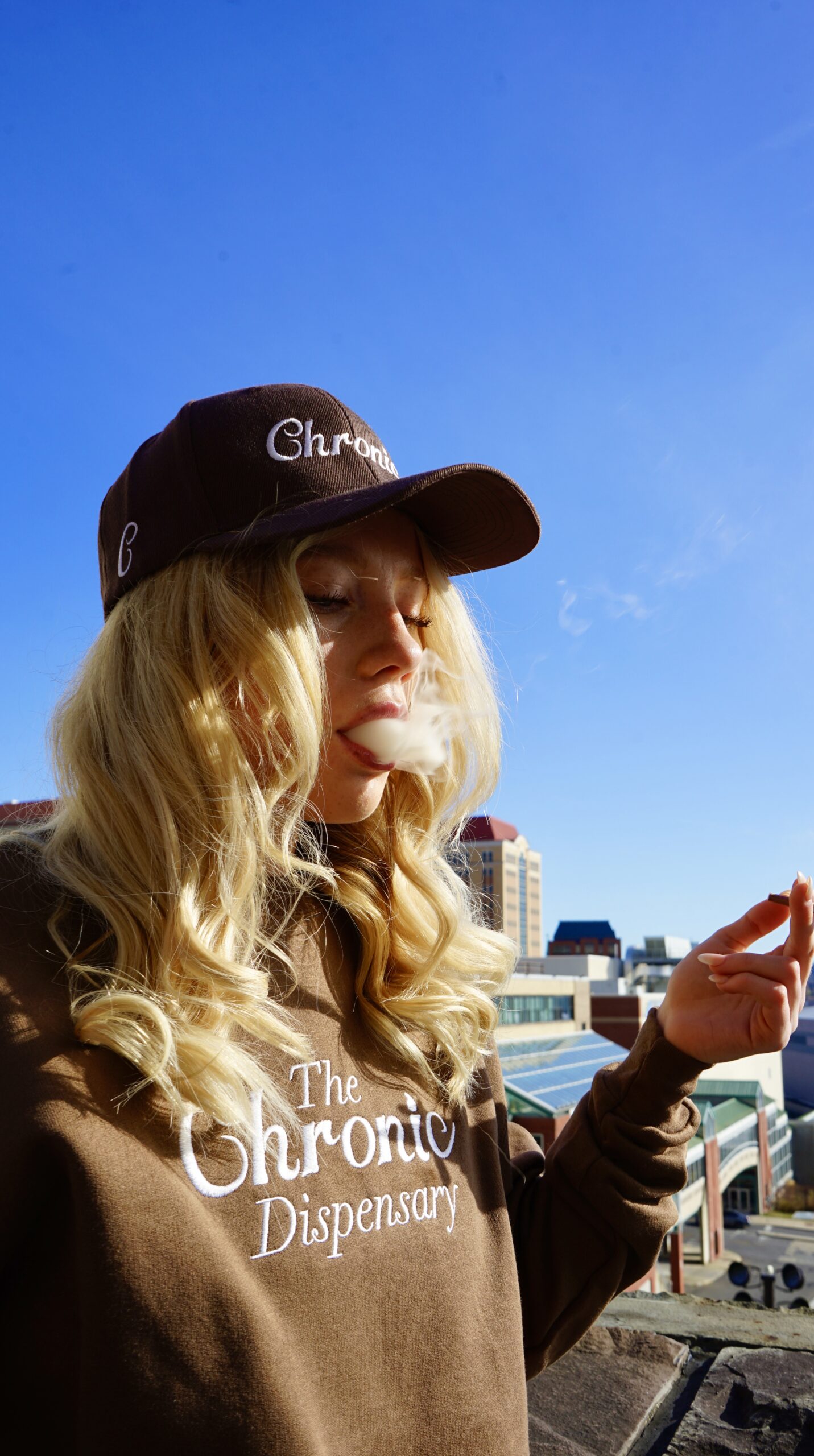 Woman outdoors smoking, wearing brown cap and sweater.